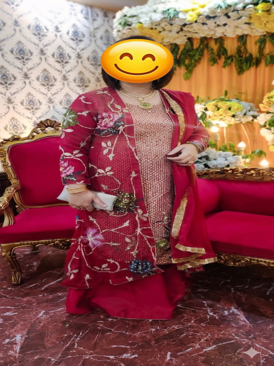 Person in a red and gold traditional outfit with floral patterns, standing in front of a decorated indoor setting.
