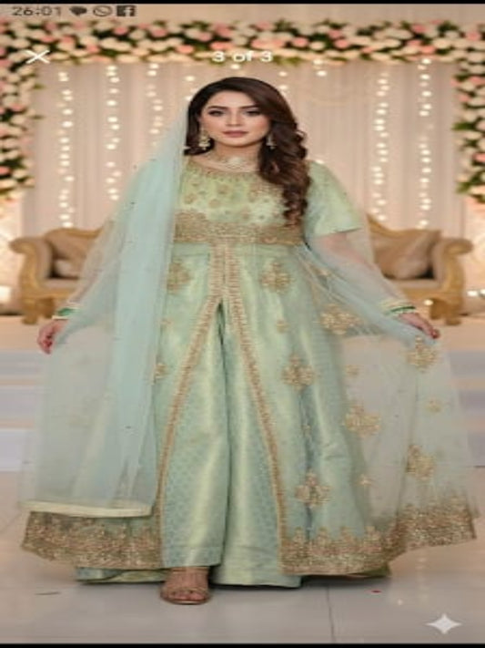 Woman in a light green traditional outfit with gold embroidery in a decorated indoor setting.
